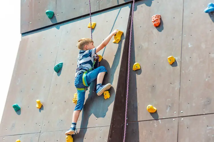 Young 7-year-old kid climbing up a bouldering wall